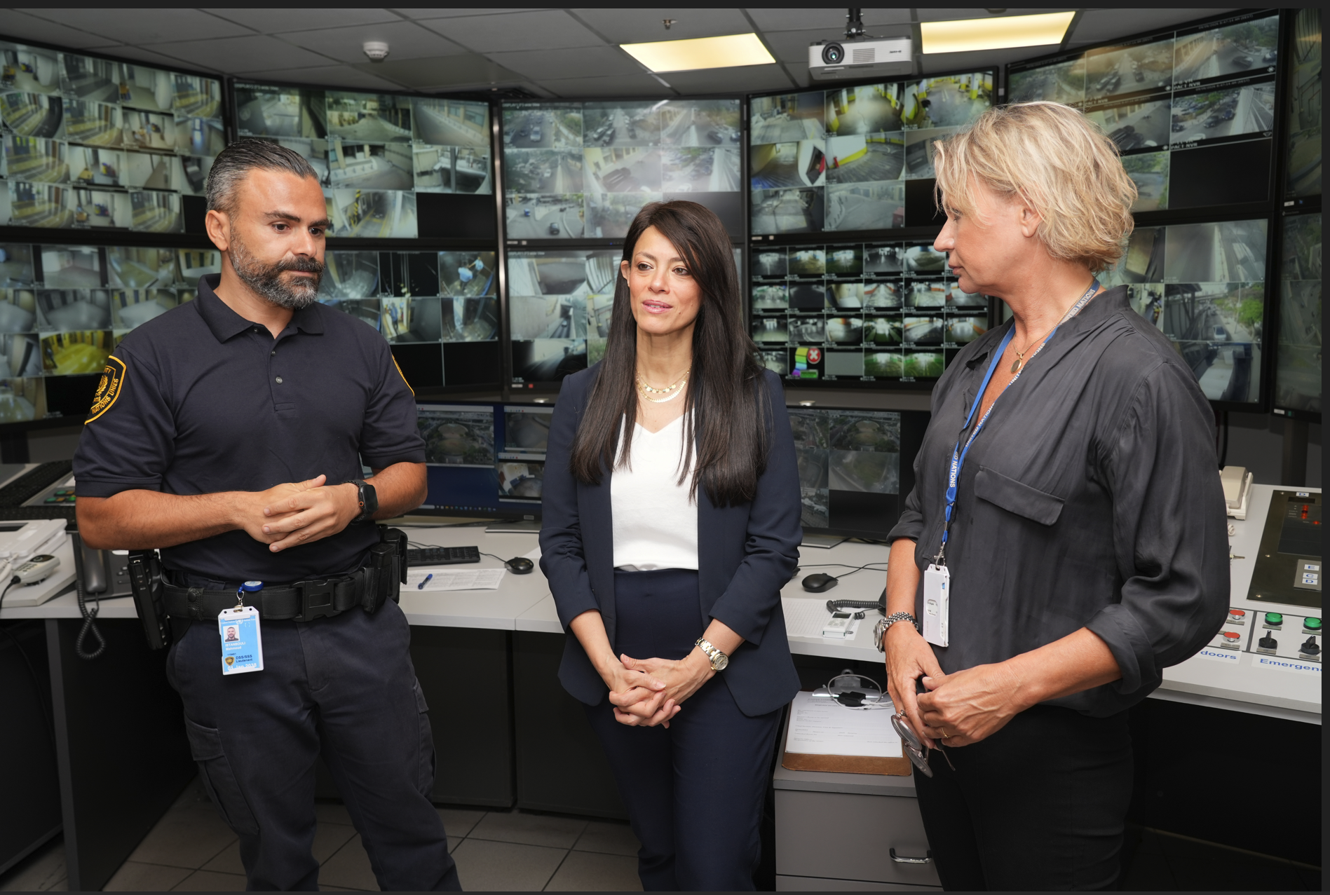 Woman standing between two security officers in a control room in front of screens