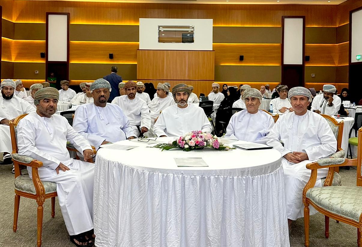Part of the audience, men around circular tables, seated in half-circle shapes, facing the podium