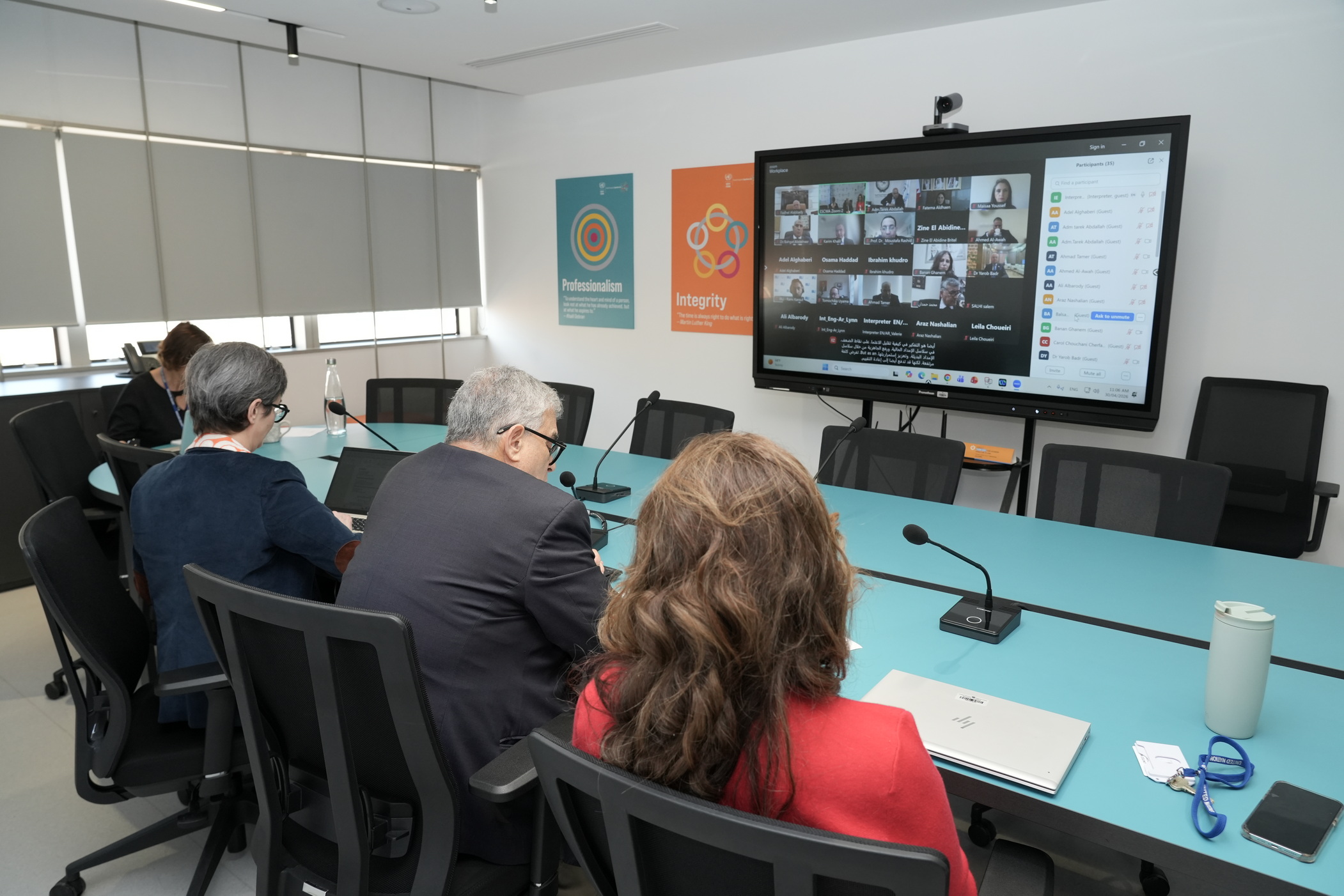 Wide shot of the room showing the back of the speakers who are facing a screen