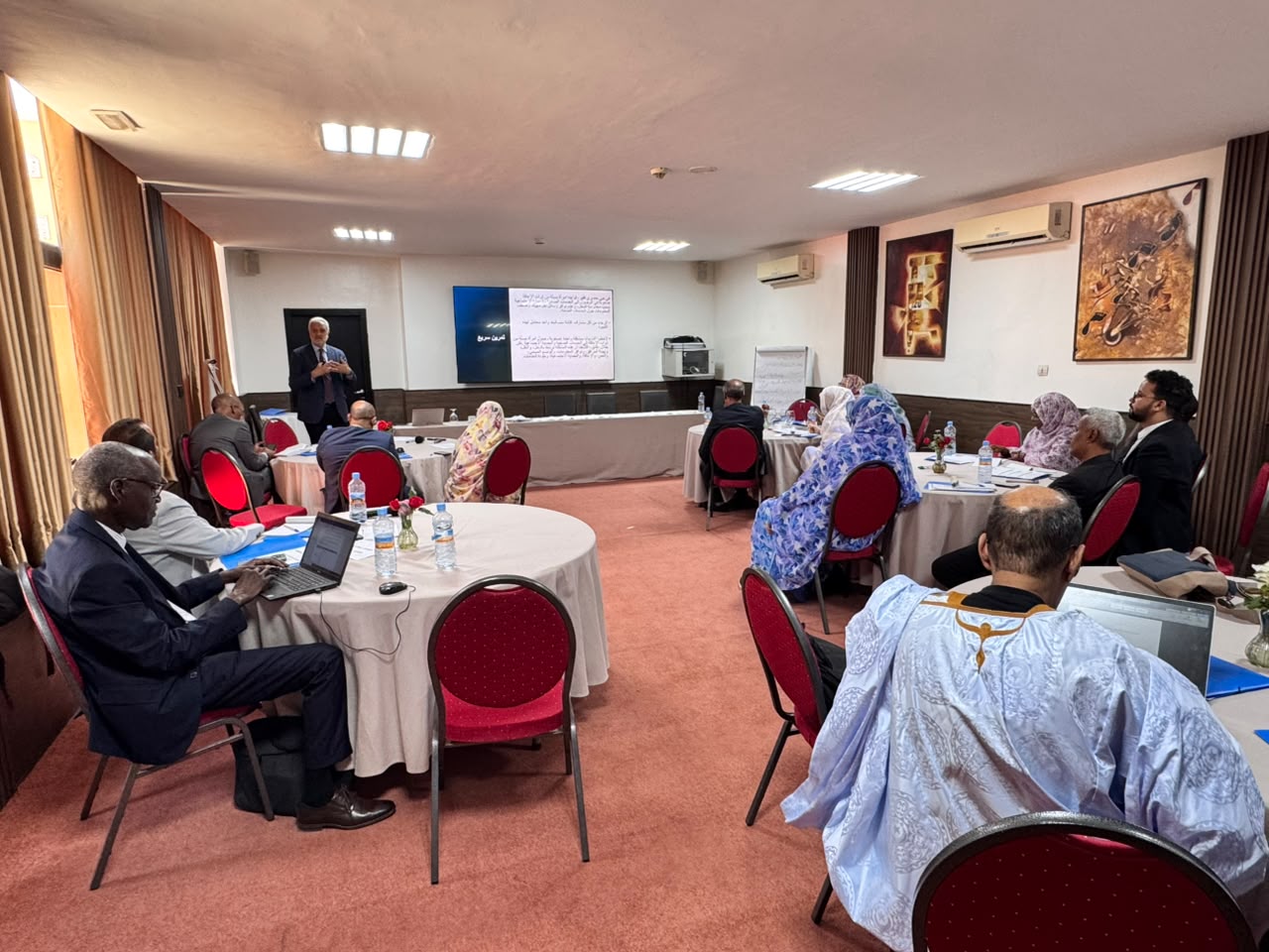 Wide shot of the room showing speaker and participants around tables