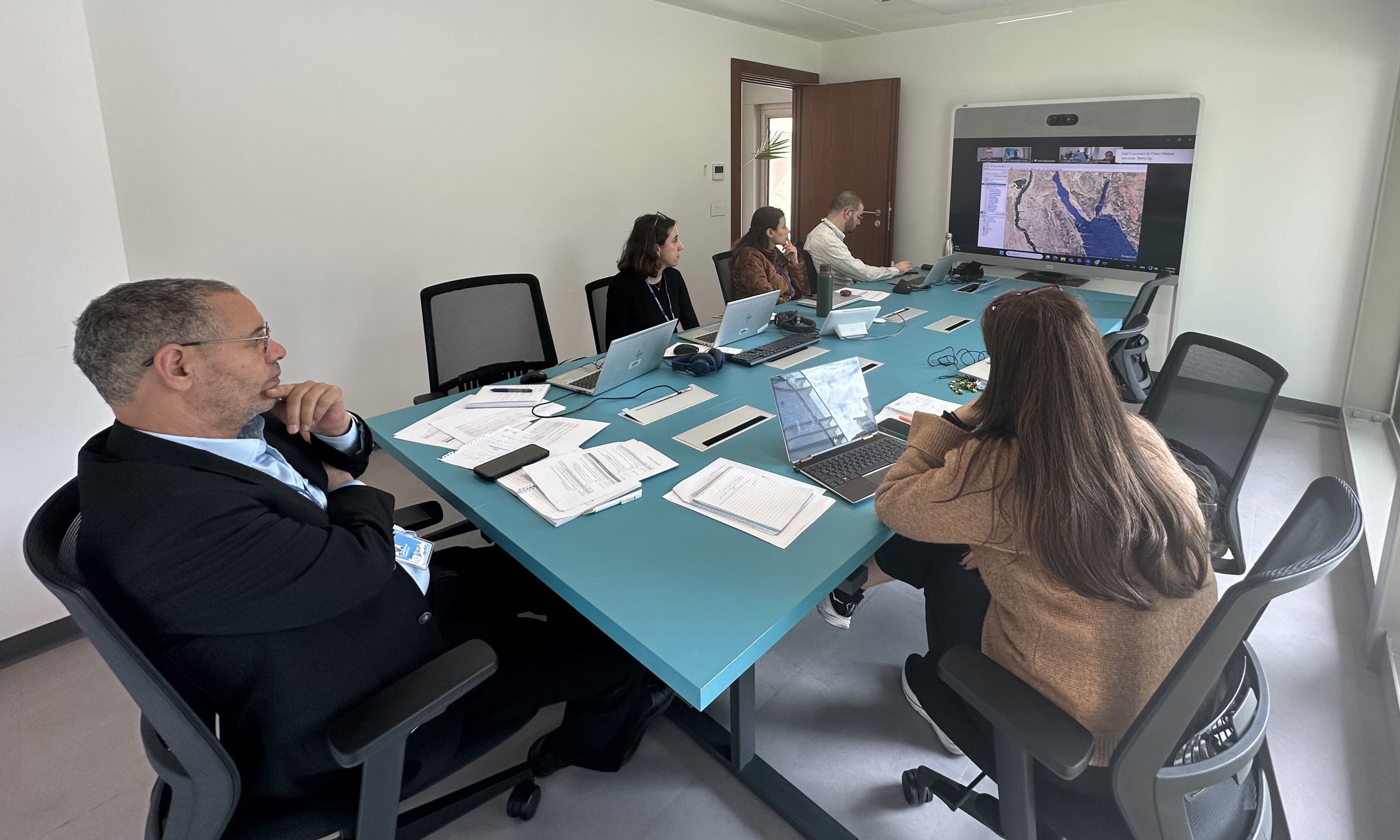 Staff seated behind a table in an office, facing a screen
