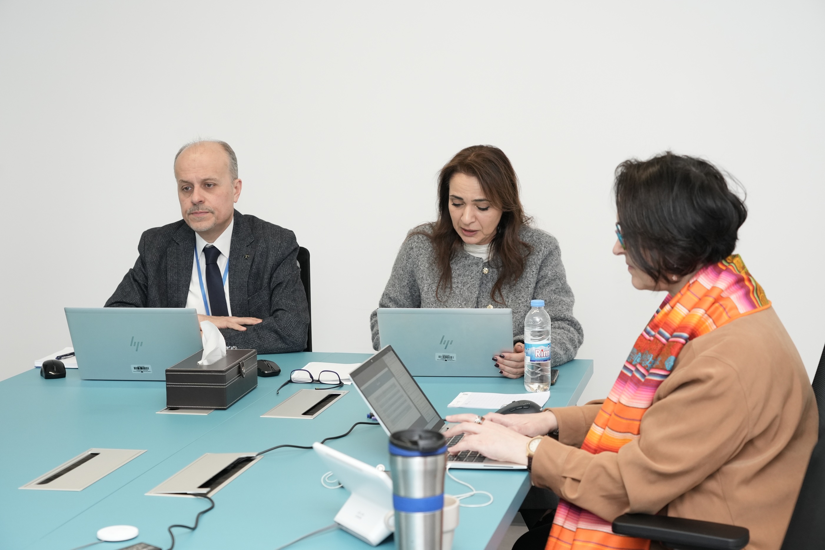 Two speakers from ESCWA sitting behind their laptops and a woman next to them taking notes on her PC