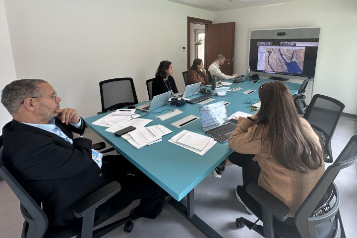Staff seated behind a table in an office, facing a screen