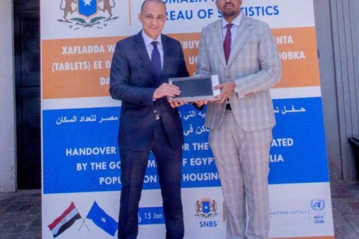 Two men standing up for the photo, handing over a tablet