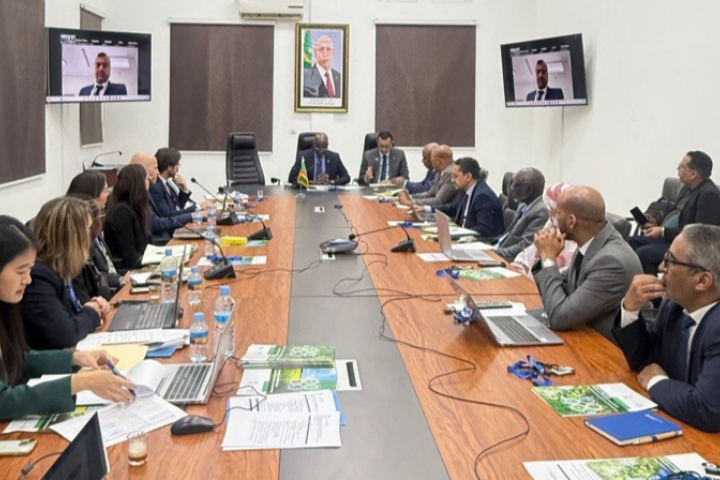 Members of two delegations seated around a table discussing with people connected online.
