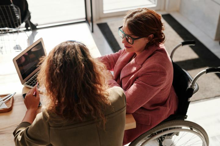 Two women sitting at a desk, one of them is on a wheelchair