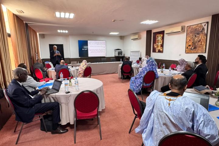 Wide shot of the room showing speaker and participants around tables